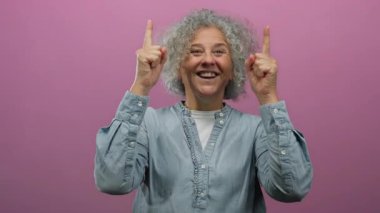 Gülümseyen, parlak pembe arka plana işaret eden, neşe ve pozitif enerji gösteren bir kadın..