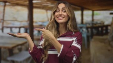 Açık avuç içi gösteren ve açık kafede gülümseyen yüzü olan genç sarışın bir kadın. Hoş geldiniz..