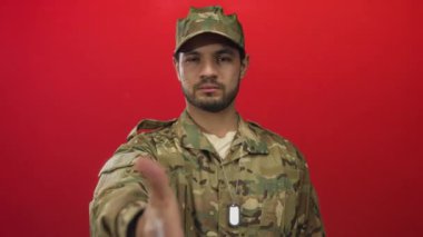 Kamuflaj üniformalı bir adam stüdyo ortamında el sıkışmak için sağ elini uzatıyor..