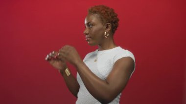 Genç Afro-Amerikalı kadın ellerini, kırmızı bir stüdyo ortamında dürbün ve emsalleri şeklinde şekillendiriyor..