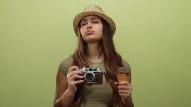 Sarı arka planda kamera ve dondurma külahı tutan İspanyol kadın şapka takıyor ve duygularını ifade ediyor. Seyahat ve eğlence teması için ideal..
