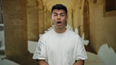 Beyaz gömlekli genç adam tarihi üniversite koridorunda duruyor ve duygularını aktarıyor..