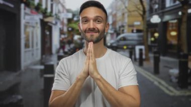 Dua eden genç adam hareketli bir şehir caddesinde gülümseyen poz veriyor. Şehir arka planında canlı bir manzara sergiliyor..