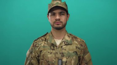 Kamuflaj üniformalı ve künyeli adam yeşil stüdyoda yumruğunu esnetti..