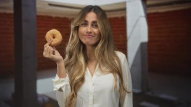 Kadın inşaat sahasında parmaklarının arasında donut tutuyor; hoşgörü oyunculuğu keyfi.