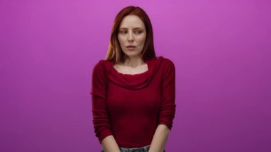 Kızıl saçlı kadın canlı pembe bir arkaplan karşısında yalnız duruyor. Neşeli bir ifadeyle ruh halini ve tarzını vurguluyor..