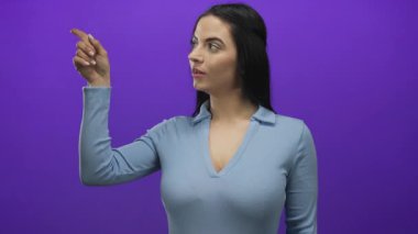 Kendine güvenen bir yüz ifadesiyle, parlak mor bir arka plana bakan açık mavi bir bluz giyen, canlı ve çekici bir anı yakalayan bir kadın..