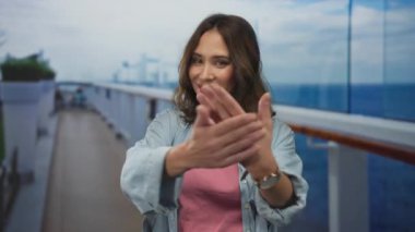 Bir yolcu gemisinin güvertesinde gülümseyen bir kadın, arka planda deniz, güneşli bir günün tadını çıkarıyor, tatilde neşe ve rahatlık sergiliyor..