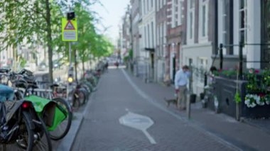 Bisikletler ve tarihi mimariyle dolu büyüleyici bir Amsterdam caddesinde köpeği gezdiren bir adam ve kadının bulanık görüntüsü..
