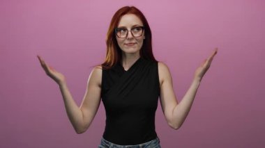 Kızıl saçlı, kendine güvenen, gözlüklü, kolları açık, zarif, şık, siyah bluzlu, soyutlanmış pembe bir arka plana karşı duran bir kadın..