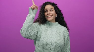 Naneli süveter giyen bir kadın canlı pembe bir duvara işaret ediyor. Tecrit edilmiş bir stüdyo ortamında gençlik hisleriyle neşe ve pozitifliği ifade ediyor..