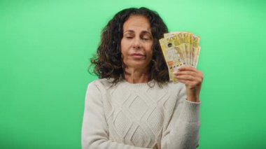 Filipinli orta yaşlı bir kadın yeşil bir duvara peso banknotlar tutuyordu. Sıkılmış ve dalgın görünüyordu..