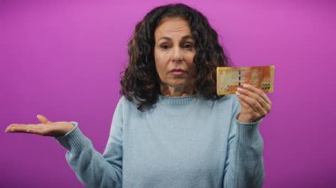 Orta yaşlı kadın, izole edilmiş mor bir geçmişe karşı kafa karıştırıcı bir ifadeyle Güney Afrika banknotunu elinde tutuyor. Bu da para yönetimi ile ilgili kafa karışıklığını simgeliyor..