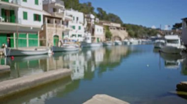 Sakin suları yansıtan teknelerle sakin liman manzarası, parlak mavi bir gökyüzünün altında Cala figera, mallorca 'da bulanık kıyı mimarisi.