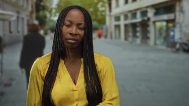 Gözleri kapalı ve sarı tişörtlü bir kadın şehir caddesinde kollarını kavuşturmuş, şehir içinde derin derin düşüncelere dalmış, geçmişi bulanık bir kadın..