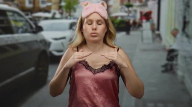 Pembe gecelikli bir kadın şehir sokaklarında uyku maskesi takarken sakinleşiyor, şehir arabalarıyla çevrili ve açık hava manzarası oluşturan hareketli bir atmosfer..