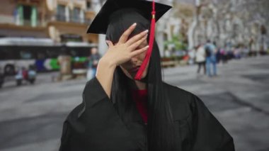 Mezuniyet kıyafetli genç İspanyol kadın şehir sokaklarında dikiliyor, endişeli görünüyor, bulanık bir şehir geçmişi var, başarıyı ve belirsizliği simgeliyor..