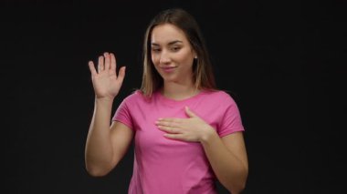 Pembe tişörtlü genç sarışın kadın içtenlik ve bağlılık jesti olarak izole edilmiş siyah bir geçmişe karşı yemin ediyor..