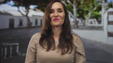 Açık havada el ele uzanan bir kadın, açık gökyüzü altında kendine güvenle gülümseyen ağaçlarla ve evlerle çevrili hoş geldin jestleri yapan bir kadın..