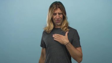 Stüdyoda eli göğsünde olan sarışın bir adam odaklanmış bakışlarını ve ince duruşunu gösteriyor..