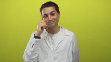 Genç İspanyol bir adam, parlak sarı bir arkaplan üzerinde parmaklarıyla düşünceli bir şekilde el kol hareketi yapıyor, günlük beyaz bir gömlek giyiyor ve anlamlı bir gülümseme takınıyor.