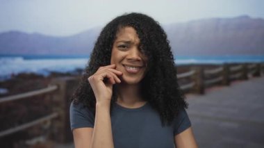 Kadın, yumuşak sabah ışığı altında sahil caddesinde anlamlı el hareketleriyle saçlarını savuruyor..