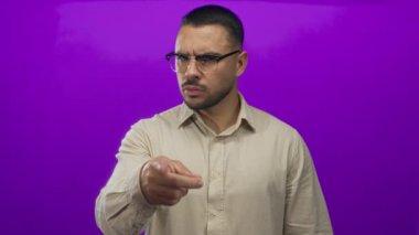 Genç İspanyol gözlüklü adam parlak mor stüdyoyu işaret ediyor; kararlılık odaklı otorite.