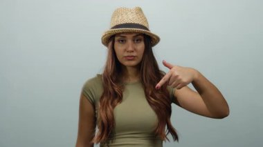 Şapka takan genç bir kadın iki eliyle aşağı doğru bakıyor. Beyaz arka plana karşı izole edilmiş. Yön ve talimatları işaret ediyor.