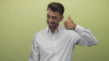 Adam gülümsüyor ve açık yeşil stüdyoda beyaz gömlekli ve kendinden emin bir ifade sergiliyor..