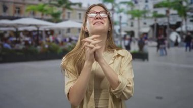 Elleri sımsıkı bağlı bir kadın, hareketli bir açık hava kafedeki restoran terasına bakıyor, umarım minnettardır..