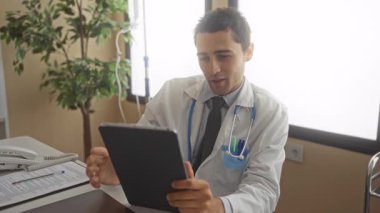 Genç İspanyol doktor kapalı bir hastane kliniğinde steteskoplu üniforma giyip tablet kullanıyor..