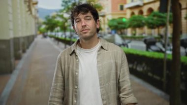 Hispanik bir adam hareketli bir sokakta, şık giyinmiş ve doğal çevresi olan bir şehir ortamında yakışıklı bir yüz ifadesi sergiliyor..