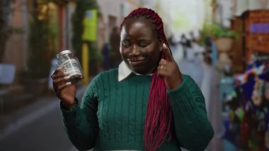 Afro-amerikalı bir kadın, açık havada içinde banknot bulunan bir kavanozu tutarken gülümsüyor. Finansal planlama ve öngörü öneriyor..