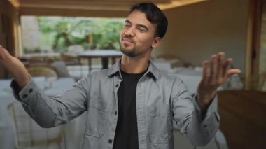 Lokantadaki genç adam güvenle gülümsüyor, kolları açık, rahat bir yemek ortamında hoş bir atmosfer yaratıyor..