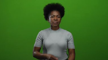 Yeşil arkaplana karşı güvenle poz veren kadın, minimalist stüdyoda gücünü somutlaştırıyor. Odaklanma ve güç, izole bir ifade ve tarzla gösteriliyor..