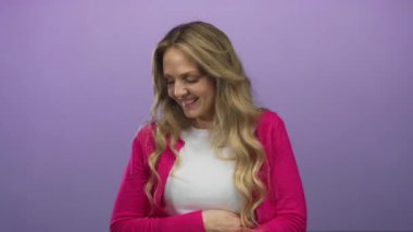 İzole edilmiş mor arka planda gülümseyen bir kadın, sarı saçlı ve pembe hırkalı, neşe ve mutluluk dolu bir kadın..