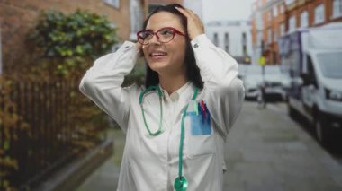 Steteskop ve üniforma giyen genç İspanyol doktor cebinde kırmızı gözlük ve kalemlerle şehir sokaklarında gülümsüyor..