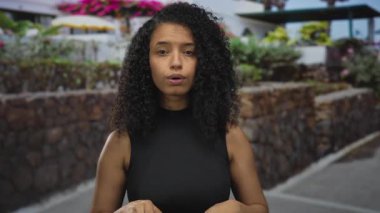 Genç İspanyol kadın taştan duvarın yanında açık avuçlar ve gün ışığında çiçek açan çalılar gösteriyor..