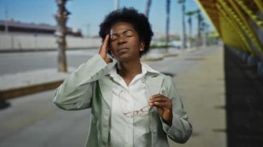 Şehir caddesindeki bir kadın, sarı bir yapının ve ağaçların yanında duran, sıkıntılı, ceketli gözlüklü bir gözlük tutuyor..