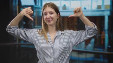 Beyaz çizgili tişört giyen genç bir kadın, binalarda iki kez baş parmak kaldırıyor. Onaylanmıyor..