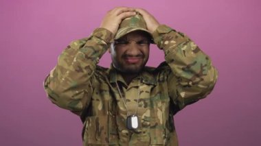 Kamuflaj üniformalı genç İspanyol asker pembe stüdyoda gümüş künye tutuyor ve alnına pembe künye yapıştırıyor..