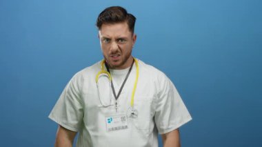 Genç sakallı doktor steteskopla poz veriyor. İzole edilmiş mavi duvar arka planına karşı bir jest yapıyor..