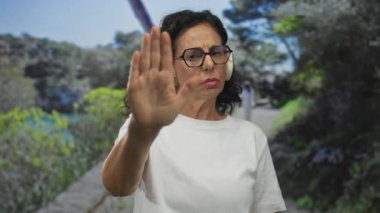 Orta yaşlı İspanyol kadın yeşil bir park yolunda avucunu kaldırıyor; sınırlara saygı.