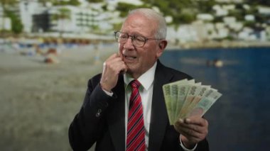 Deniz kıyısında bir kumsalda elinde Czech Koruna banknotları tutan kıdemli bir adam, takım elbise giyiyor, su kenarındaki fırsatları ve refahı yansıtıyor..