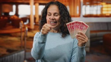 Otel resepsiyonunda orta yaşlı bir kadın İsrail şekellerini gösterirken, para birimi için neşeli bir ifade ve coşku sergiliyor..