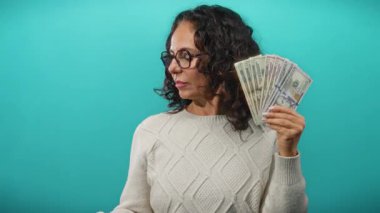 Amerikan dolarlarını elinde tutan orta yaşlı bir kadın izole edilmiş mavi bir geçmişe karşı düşünceli bir ifadeyle mali kararları ve zenginliği sembolize ediyor..