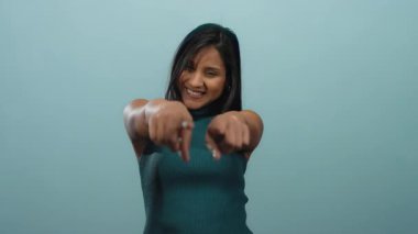 Bir kadın mavi arka planda gülümserken parmaklarıyla zafer jesti yapıyor.