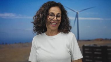 Yel değirmeniyle tarlada gülümseyen, gözlük takan ve işaret eden, yenilenebilir enerji ve açık hava yaşam tarzını temsil eden bir kadın..