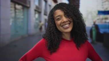 Meşgul şehir caddesinde görünen dişleri ve kıvırcık saçlarıyla gülümseyen, kalçaları üzerinde elleri olan, kendine güvenen bir kadın..