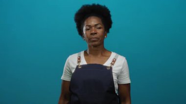 Önlüklü kadın, gürültüye karşı kulaklarını kapatır. Mavi arka planda, yüksek sesli ve rahatsız edici seslere tepki olarak hayal kırıklığına uğramış ya da sıkıntılı görünür..